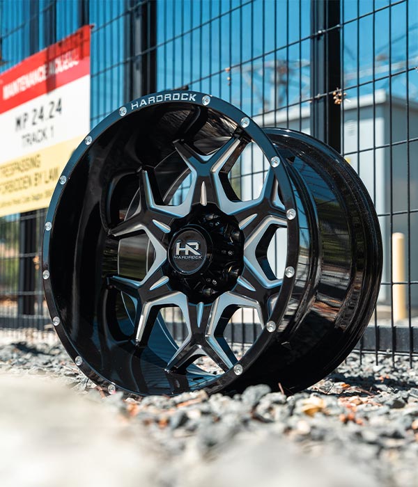 gloss black milled h507 off road wheel on rocks against a black wire fence