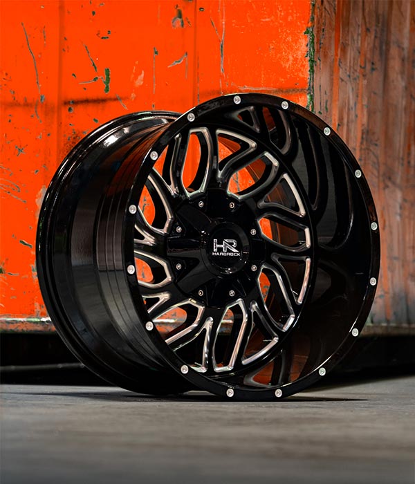 gloss black milled hardrock offroad h707 truck wheel on concrete floor with bright orange cargo container behind it