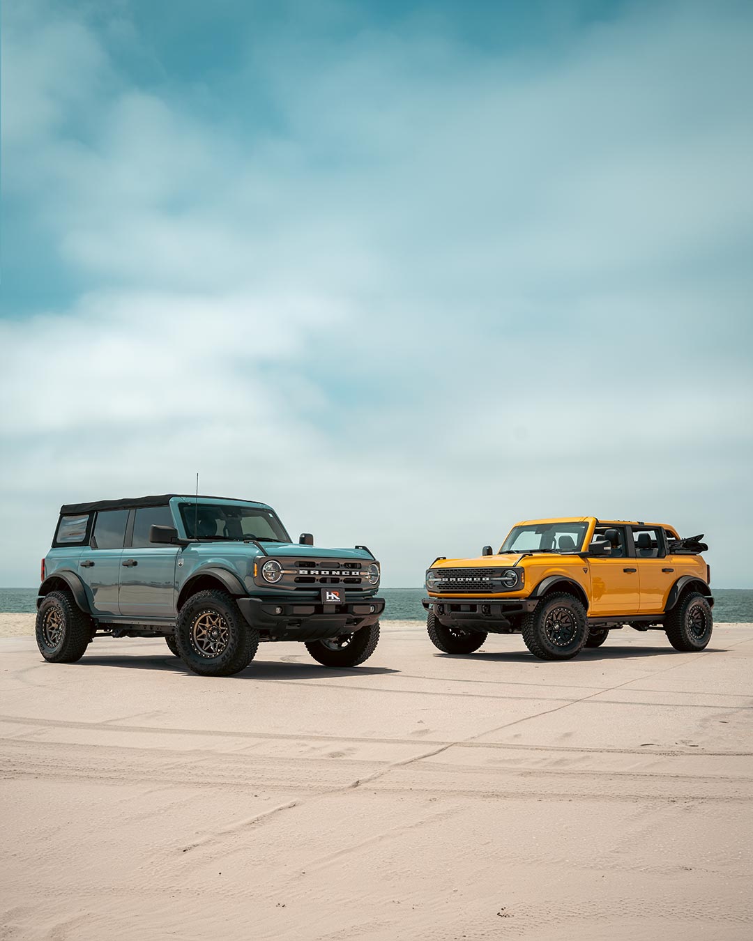 two ford broncos by the ocean with beach sand in the foreground