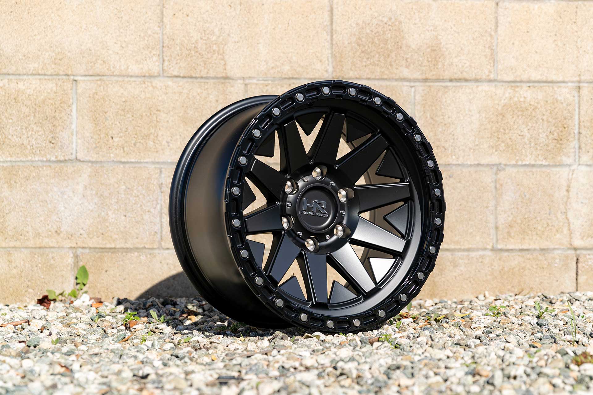 matte black hardrock offroad h106 on gravel set against a light-colored concrete brick wall