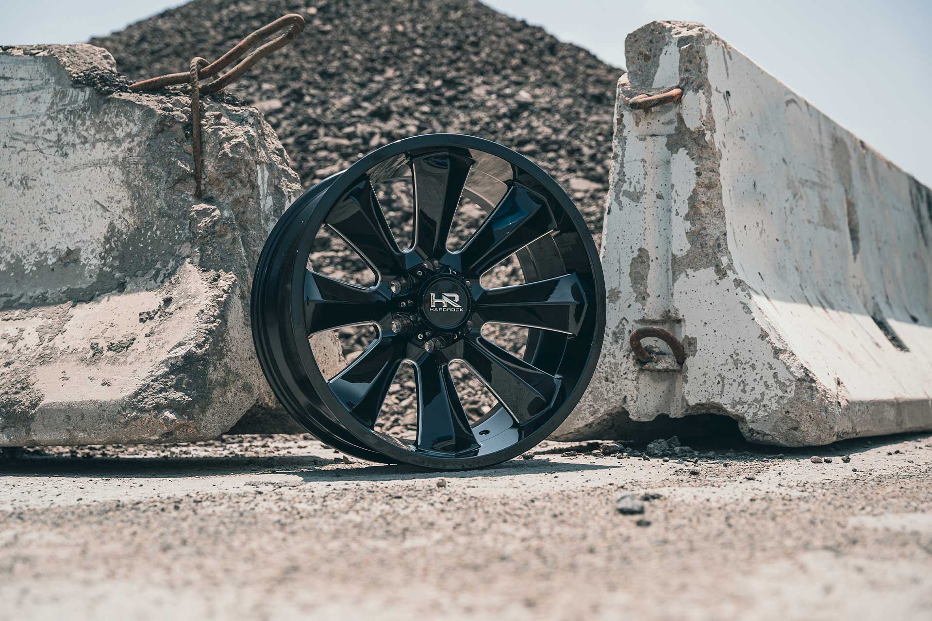 gloss black machined hardrock offroad h506 on gravel next to concrete barrier walls and rocky hill