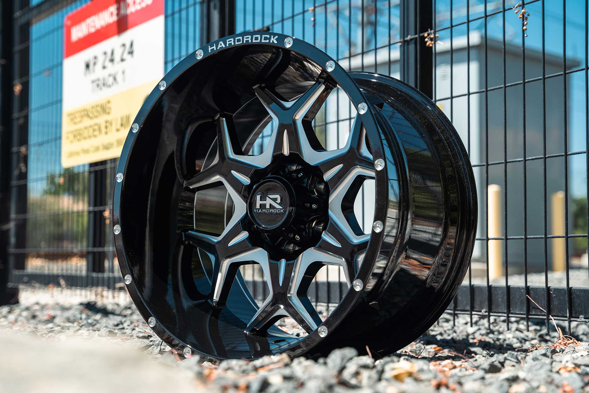 gloss black machined hardrock offroad h507 on gravel next to black wire fence