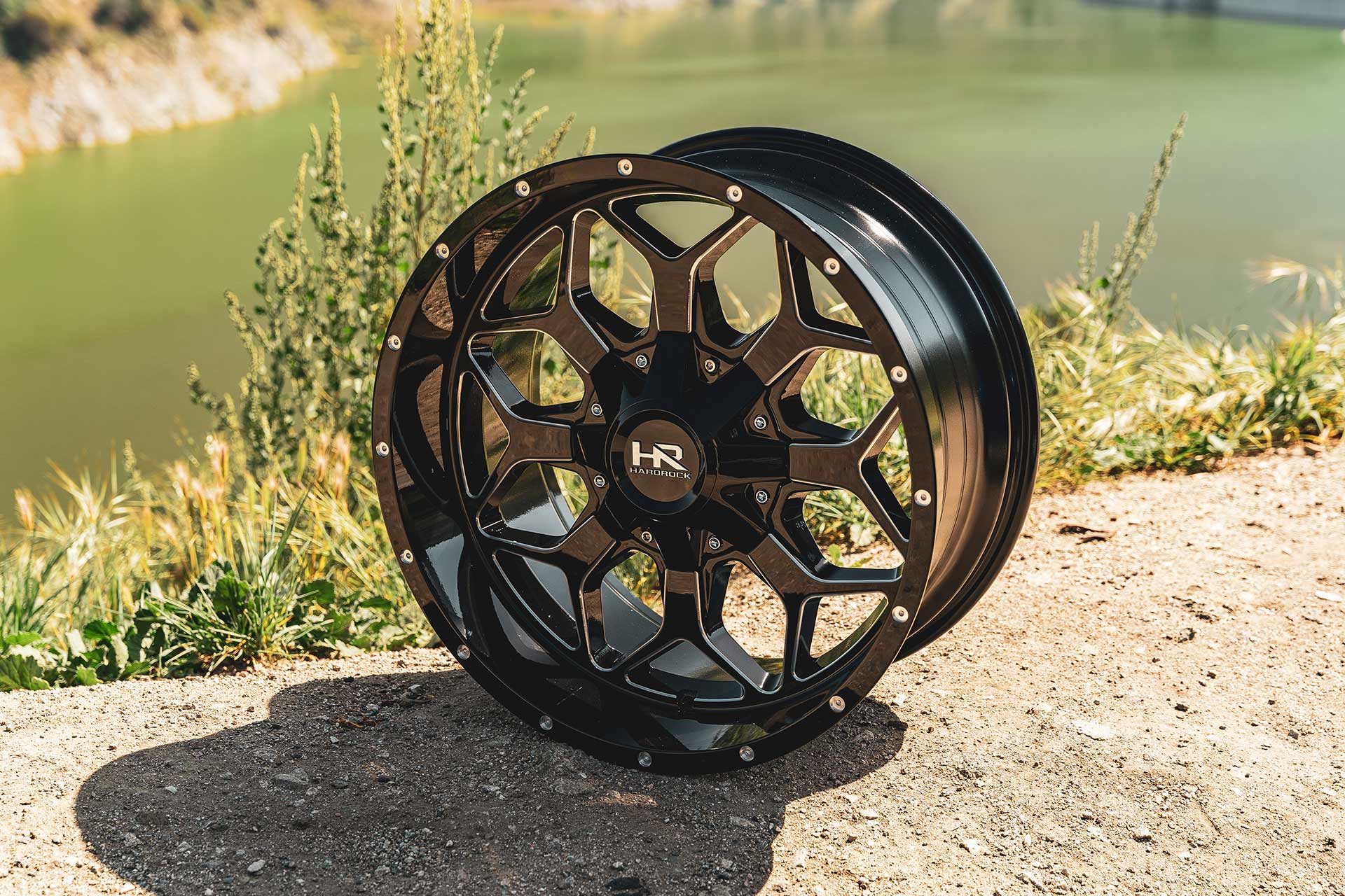 gloss black machined hardrock offroad h712 on sandy surface with body of water behind it