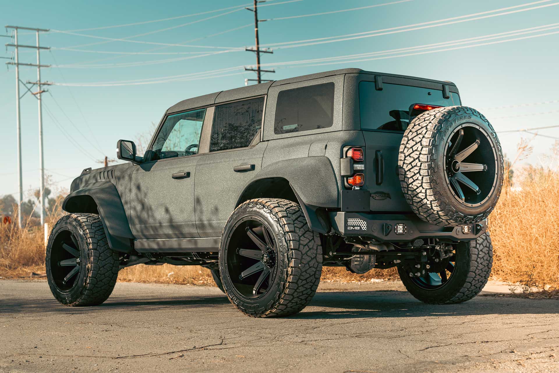 liner sprayed ford bronco bronco raptor with satin black hardrock offroad h502 truck wheels in an industrial scene with dirt and rocks