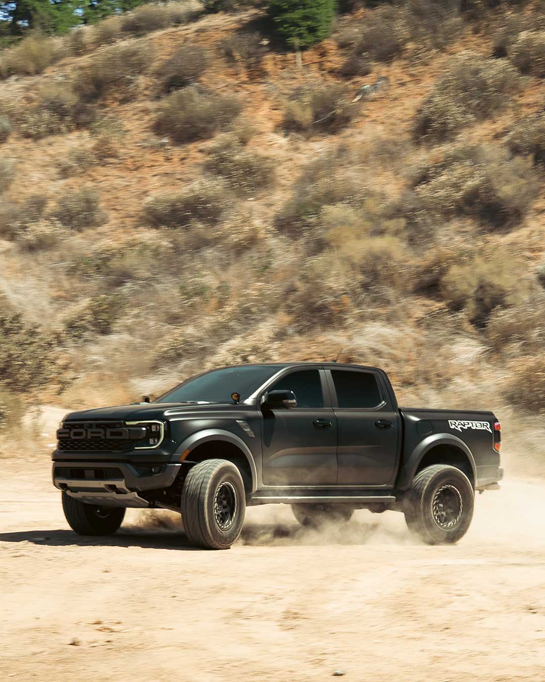 off road driving shot of a matte black ford ranger raptor with matte black off road wheels and off road tires