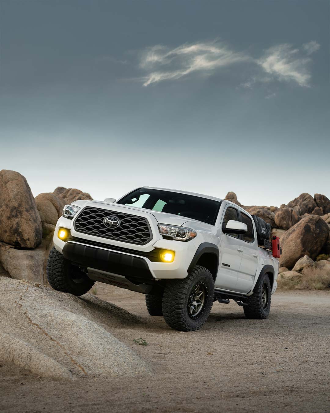 white overland toyota tacoma flexing suspension on rock in desert